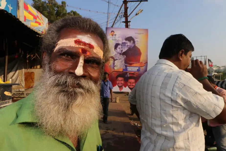Man with ceremonial paint on his face in front of a sign about dating in India