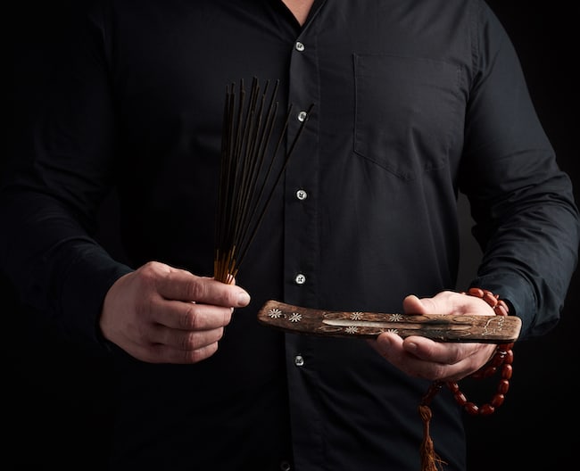 adult man in black clothes holds a stack of incense sticks