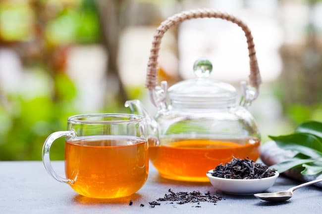 Black tea in glass cup and teapot on summer outdoor background. Copy space.