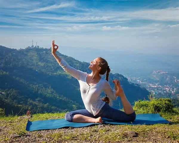 Yoga outdoors - young sporty fit woman doing stretching yoga asana Eka pada rajakapotasana - one-legged king pigeon pose in Himalayas mountains, India